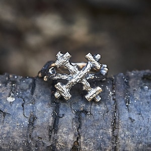 Peut inclure: Une bague en argent avec un motif de flocon de neige. La bague est en métal et a un aspect rustique et organique.