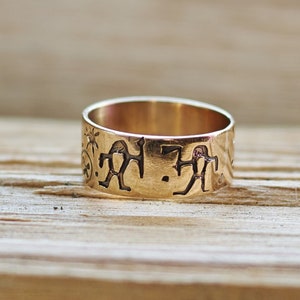 May include: A gold band ring with an inscription of stylised figures and symbols.