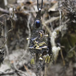 Close-up view of a mixed metal witch pendant with a blue lapis lazuli cabochon, detailed witch on broomstick, crescent moon, and cat familiar charms, showcasing intricate craftsmanship.