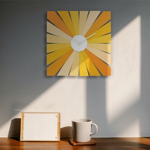 May include: A yellow and orange sunburst wall clock with white hands and a white face. The clock is hanging on a gray wall.