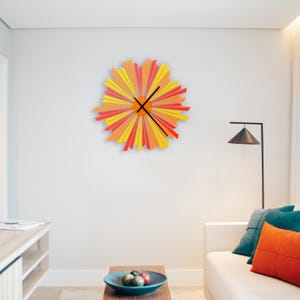 May include: A large, colourful wall clock with a sunburst design. The clock has red and yellow stripes radiating out from the centre. The clock hands are black.
