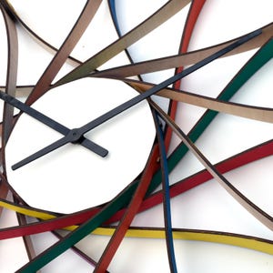 May include: A colourful clock with a white face and black hands. The clock is made of multiple strips of wood, each painted a different colour, and arranged in a radial pattern.