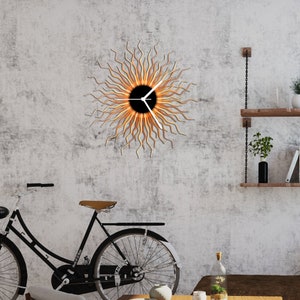 May include: A modern wall clock with a sunburst design. The clock face is black with white hands and a gold rim. The sunburst is made of thin, wavy metal pieces in shades of orange and yellow.