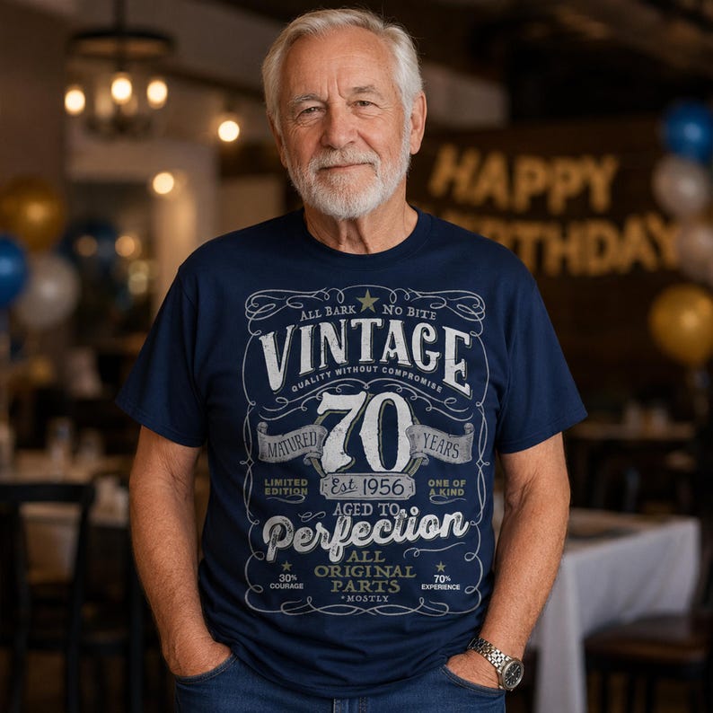 May include: A navy blue t-shirt featuring a white graphic design with the text Vintage 70 Years Matured Aged to Perfection Est 1956 All Original Parts. The print includes decorative scrollwork, stars, and various phrases in a vintage-style layout.