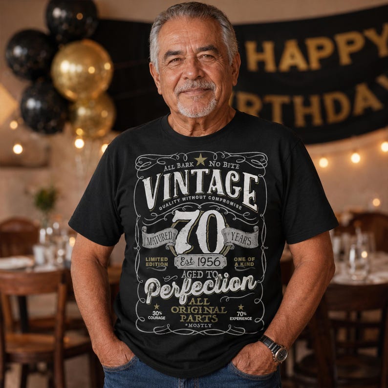 May include: A black t-shirt featuring a white graphic design with the text "VINTAGE 70 YEARS MATURED EST 1956 AGED TO PERFECTION ALL ORIGINAL PARTS". The design includes decorative scrollwork, stars, and various phrases in a vintage-inspired layout.