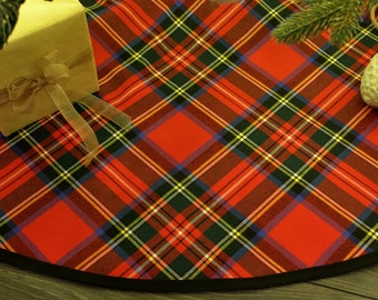 以下が含まれることがあります： 黒の縁取りが付いた赤と緑のタータンチェックのクリスマスツリースカート。スカートの上に、金のリボンで結ばれた茶色の包み紙で包まれたプレゼントが置かれています。スカートの上に、松の枝と白い松ぼっくりも置かれています。