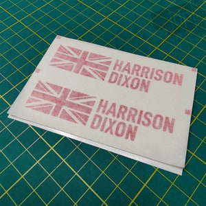 K&ouml;nnte beinhalten: Zwei wei&szlig;e Bl&auml;tter Papier mit rot gedruckten Union Jacks und dem Text "HARRISON DIXON", der zweimal wiederholt wird.