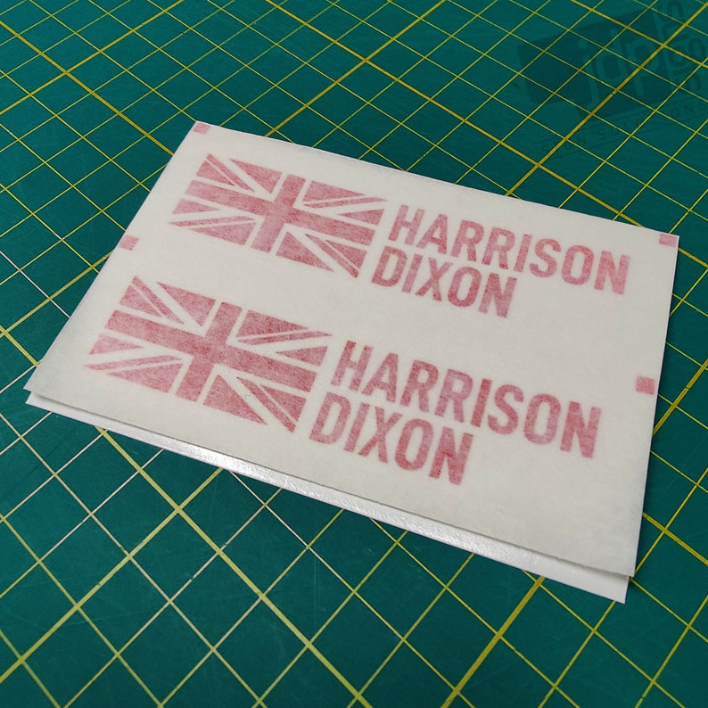 K&ouml;nnte beinhalten: Zwei wei&szlig;e Bl&auml;tter Papier mit rot gedruckten Union Jacks und dem Text "HARRISON DIXON", der zweimal wiederholt wird.