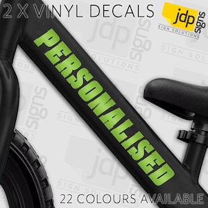 May include: Black bicycle frame with the word "PERSONALISED" in bright green vinyl lettering. The text "2 X VINYL DECALS" is at the top, and "22 COLOURS AVAILABLE" is at the bottom. The logo for "jdp signs" is in the upper right corner.