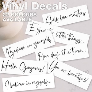 May include: White vinyl decals featuring motivational quotes in a cursive script. The phrases include "Self love matters," "Enjoy the little things," and "You are beautiful!" The text "Vinyl Decals" and "22 COLOURS AVAILABLE" are also displayed.
