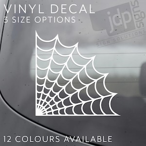 Op de afbeelding: Witte vinyl sticker met een hoekontwerp van een spinnenweb. De tekst "VINYL DECAL" en "3 SIZE OPTIONS" staan bovenaan. De tekst "12 COLOURS AVAILABLE" staat onderaan. De sticker is ontworpen voor toepassing op een autoraam.