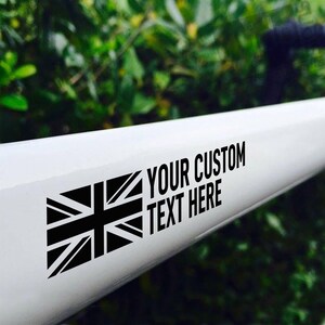 K&ouml;nnte beinhalten: Ein wei&szlig;er Fahrradrahmen mit einer schwarzen Union Jack Flagge und dem Text "YOUR CUSTOM TEXT HERE" darauf gedruckt.