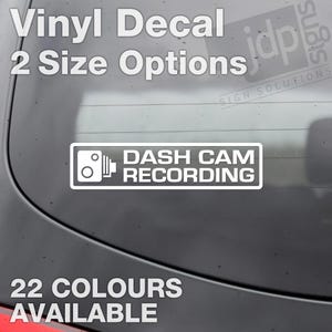 Könnte beinhalten: Weißer Vinyl-Aufkleber mit dem Text "DASH CAM RECORDING" und einem Kamerasymbol. Der Aufkleber befindet sich an einer Autoscheibe. Der Text "22 FARBEN VERFÜGBAR" befindet sich unter dem Aufkleber.
