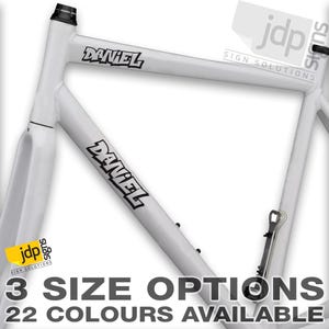 Könnte beinhalten: Weißer Fahrradrahmen mit schwarzer Beschriftung "DANIEL" auf beiden Seiten. Das Bild enthält den Text "3 SIZE OPTIONS 22 COLOURS AVAILABLE".