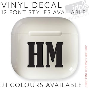 Könnte beinhalten: Ein weißes Airpods-Case mit den schwarzen Buchstaben "HM" in fetter Schrift. Der Text "VINYL DECAL", "12 FONT STYLES AVAILABLE" und "21 COLOURS AVAILABLE" sind ebenfalls sichtbar. Die Worte "AIRPODS CASE NOT INCLUDED" sind rot.