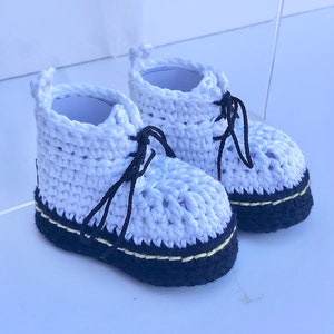 May include: A pair of white crocheted baby booties with black laces and black and yellow trim.