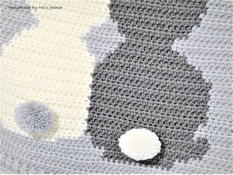 May include: A crocheted baby blanket with a yin yang design in white and gray. The blanket has two pom-poms, one white and one gray.