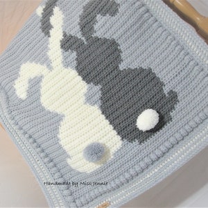 May include: A gray and white crocheted baby blanket with a design of two bunnies. The bunnies have white pom-poms for tails. The blanket has a gray border with a white trim. "Handmade by Miss Jennie" is written on the blanket.