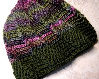 May include: A handmade knit beanie in shades of green, purple, and pink. The hat features a textured, cable-knit design with a folded brim. The color palette includes olive green, deep purple, and soft pink, creating a warm and cozy look.