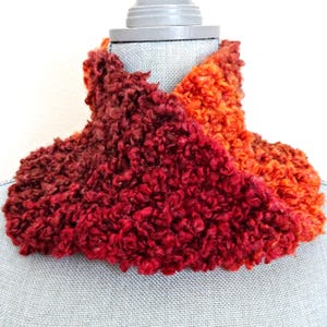 Peut inclure: Un chauffe-cou fait à la main, aux tons rouges et oranges. Le fil texturé, bouclé, crée un aspect doux et moelleux. L'écharpe est présentée sur un mannequin, mettant en valeur sa forme et son style. Un accessoire chaud pour l'hiver.