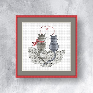 May include: Cross-stitch art of two cats, one gray with a red scarf and the other blue, sitting together. Their tails form a heart shape, and a dotted heart is above them. The artwork is framed in red and gray.