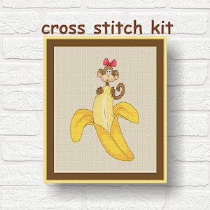 Puede incluir: Kit de punto de cruz con un mono de dibujos animados que lleva un lazo rosa, asomándose por una cáscara de plátano amarilla.