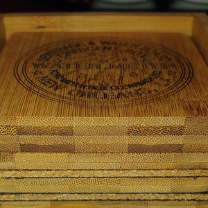 May include: A set of six bamboo coasters in a wooden holder. The coasters feature a circular design with the text "Enjoy a Waiter's Moment" and "Water, Time & Mile High Clouds".