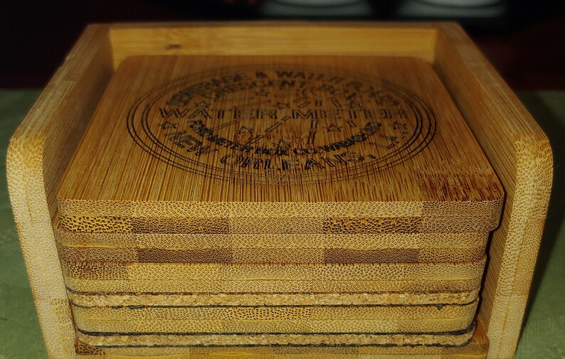 May include: A set of six bamboo coasters in a wooden holder. The coasters feature a circular design with the text "Enjoy a Waiter's Moment" and "Water, Time & Mile High Clouds".