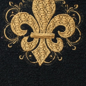May include: A gold embroidered fleur-de-lis design on a black fabric background.