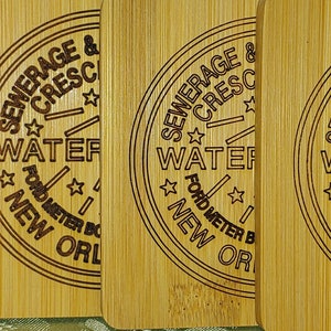 May include: Four wooden coasters with a laser-engraved design featuring the text "SEWERAGE & CRESCENT WATER" and "FORD METER BOX CO. WABASH, LA."