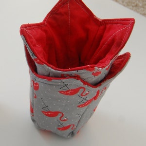 K&ouml;nnte beinhalten: Ein grauer Stoffaufbewahrungskorb mit roter Innenauskleidung. Der Korb hat die Form eines Sterns und ist mit einem Muster aus rosa Flamingos verziert.
