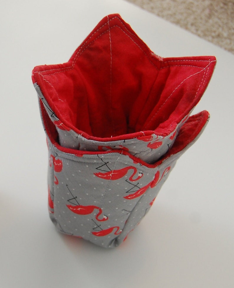 K&ouml;nnte beinhalten: Ein grauer Stoffaufbewahrungskorb mit roter Innenauskleidung. Der Korb hat die Form eines Sterns und ist mit einem Muster aus rosa Flamingos verziert.