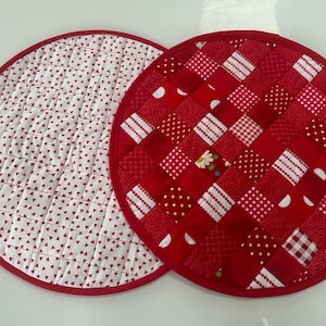 May include: Two red and white quilted pot holders. One pot holder has a patchwork design with red, white, and gingham squares. The other pot holder has a white background with small red triangles.