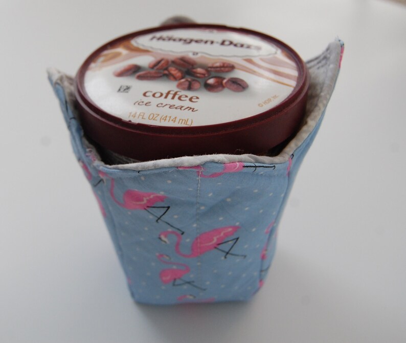 K&ouml;nnte beinhalten: Ein blauer Stoffbeh&auml;lter f&uuml;r Eis mit pinken Flamingomustern. Der Beh&auml;lter enth&auml;lt eine Packung Haagen-Dazs Kaffee-Eis.