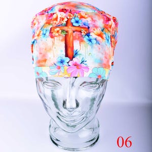 Close-up profile view of the Christian scrub cap, highlighting the detailed watercolor cross design with artistic paint splatters and blending of pink, purple, and blue hues.