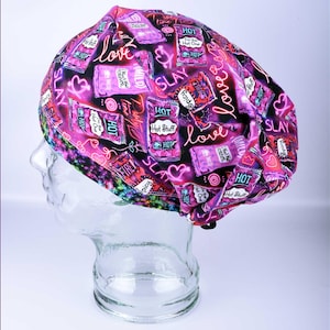 May include: A pink and purple surgical scrub cap with a repeating pattern of hot sauce packets, hearts, and the words "love" and "slay" in a neon-style font. The cap is designed to fit over the head.