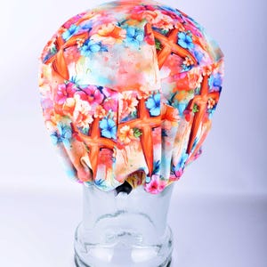 Back view of the watercolor cross patterned scrub cap on a clear mannequin head, showing the full-coverage design and the enclosed elastic band gathered neatly at the base of the neck.