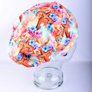 Side view of the watercolor cross patterned scrub cap on a clear mannequin head, showing the full-coverage design and the enclosed elastic band gathered neatly at the base of the neck.