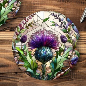 May include: Two round car coasters with a stained-glass design featuring a purple thistle flower, green leaves, and a cream-colored background. The coasters are on a wooden surface, next to a set of car keys.