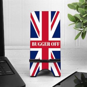 May include: A phone stand with a Union Jack design and the text "BUGGER OFF" printed on it. The stand is made of plastic and has a black base.