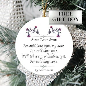 May include: White round Christmas ornament with a gold string. The ornament features a poem by Robert Burns, "Auld Lang Syne", with a floral design of purple thistles.