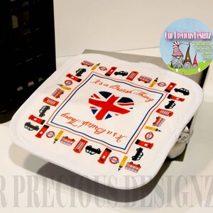 May include: White pot holder with a red, white, and blue heart with the Union Jack flag design. The text "It's a British Thing" is printed on the pot holder. The pot holder is surrounded by a border of red telephone booths, double-decker buses, and other London-themed icons.