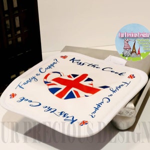 Könnte beinhalten: Ein weißer Topflappen mit einem Union-Jack-Teekannen-Design und dem Text "Fancy a Cuppa? Kiss the Cook & Fancy a Cuppa? Kiss the Cook".