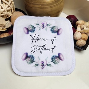 May include: White cotton pot holder with a purple and green thistle design and the text "Flower of Scotland".