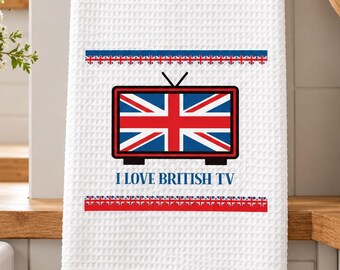May include: A white waffle-textured kitchen towel hanging on a rod. The towel features a graphic of a television set displaying the Union Jack flag, with the text I LOVE BRITISH TV printed below it, framed by two horizontal rows of small flag icons.