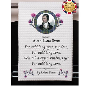 Puede incluir: Una toalla de cocina blanca con un retrato de Robert Burns y la letra de la canción "Auld Lang Syne". La toalla tiene un patrón de tartán y un diseño floral.