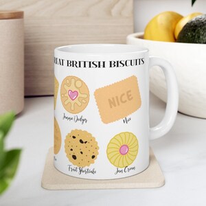 May include: White ceramic mug with a design of different British biscuits, including a Jammie Dodger, a Nice biscuit, a Fruit Shortcake, and a Jam Cream. The text "Great British Biscuits" is printed on the mug.