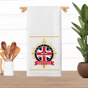 May include: White kitchen towel with a gold and red design featuring the Union Jack flag and the text "Proud to be British".