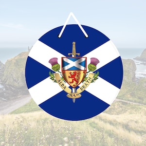 Puede incluir: Una bandera escocesa redonda, azul y blanca, con una cruz blanca y un escudo de león dorado en el centro. El escudo está rodeado por una cinta blanca con las palabras "Alba Gu Brath" en letras doradas.