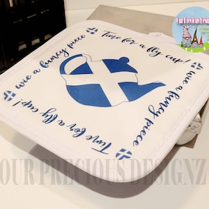 Könnte beinhalten: Ein weißer Topflappen mit einem blau-weißen skandinavischen Flaggenmuster. Der Text "Time for a fly cup!" und "I wie a funcy piece" ist auf dem Topflappen geschrieben.